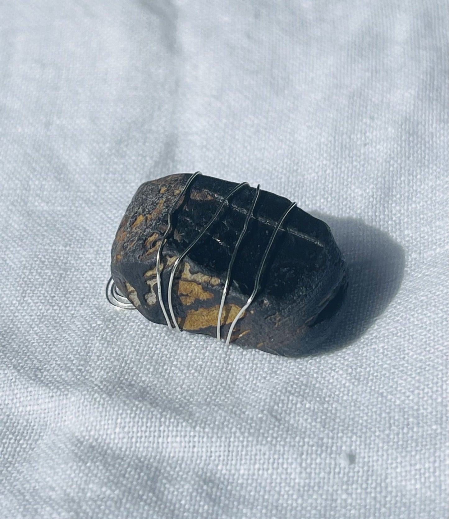 A rich brown Wise Rock pendant wrapped in silver-coloured wire, showcasing earthy tones and unique patterns