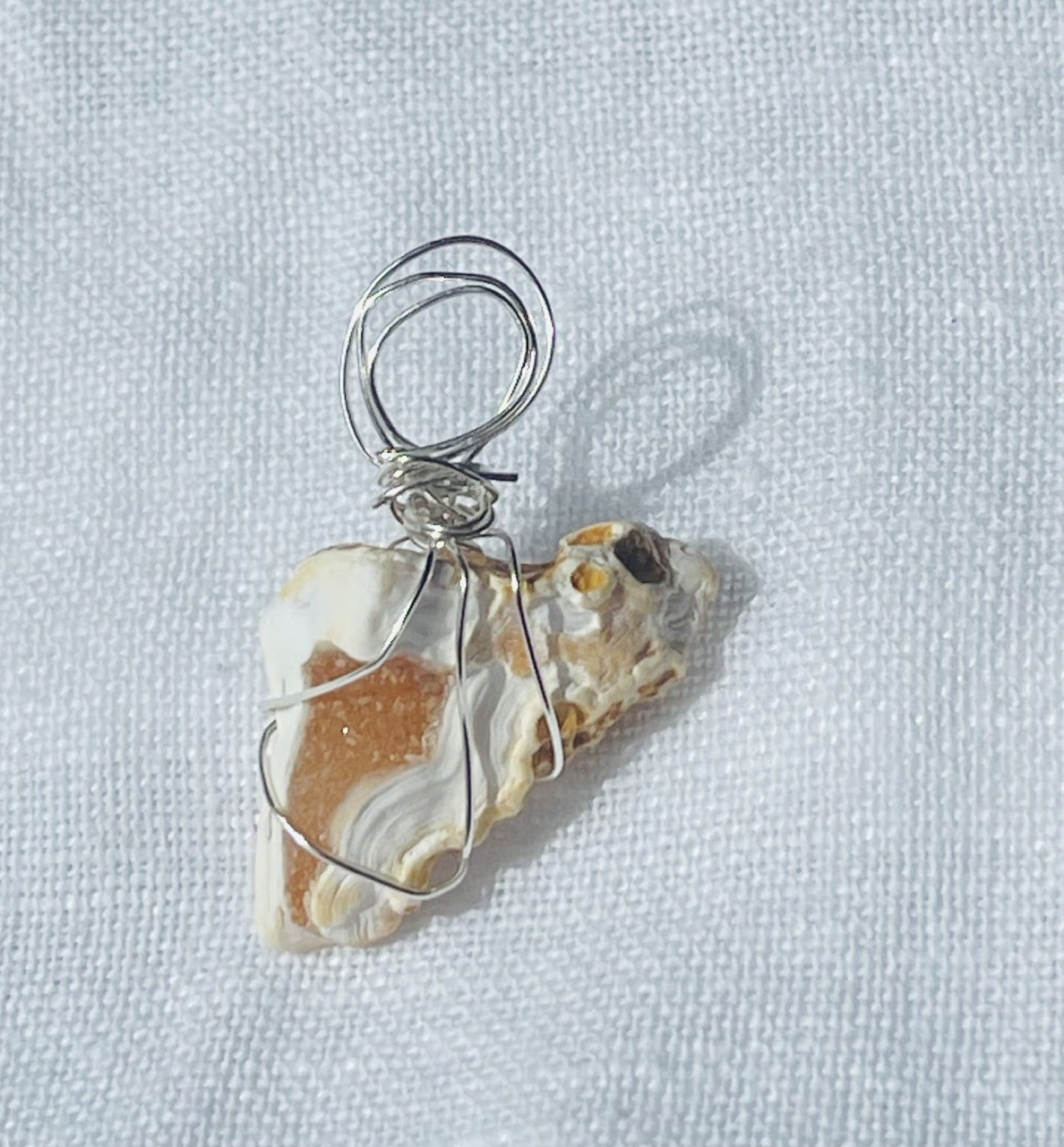 A soft white Wise Rock pendant with a captivating orangey geode center, wrapped in silver-coloured wire, showcasing timeless elegance and subtle radiance