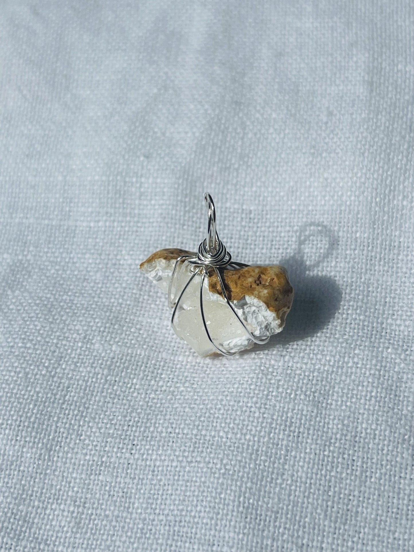 A silver-wrapped pendant with shimmering sparkles, chalky cave-like whites, and translucent tones, reminiscent of moonlit water