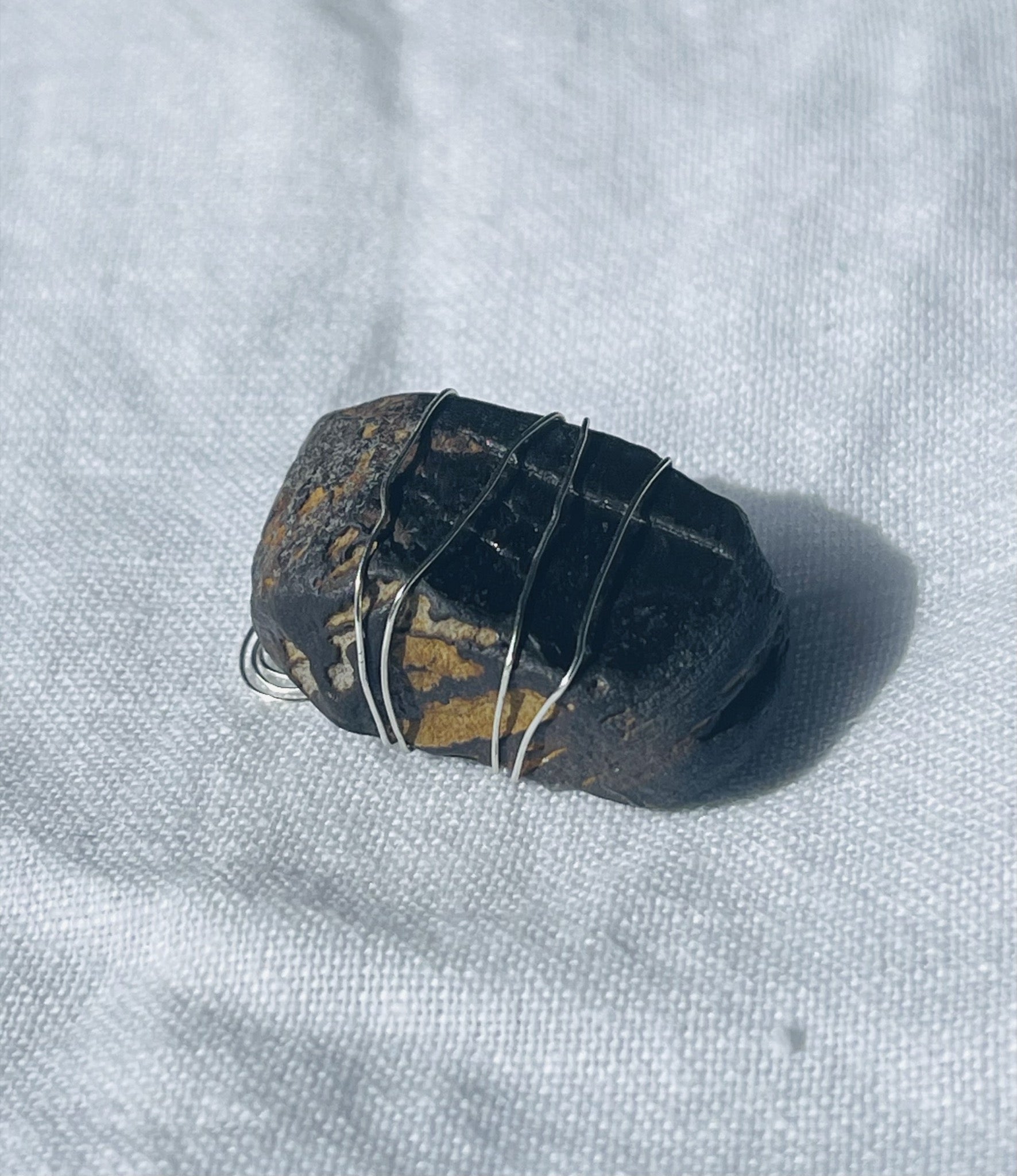 A rich brown Wise Rock pendant wrapped in silver-coloured wire, showcasing earthy tones and unique patterns